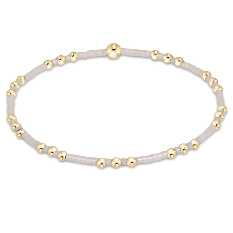 A delicate beaded stretch bracelet featuring light gray translucent beads and polished gold-tone spacer beads, displayed on a clean white background.