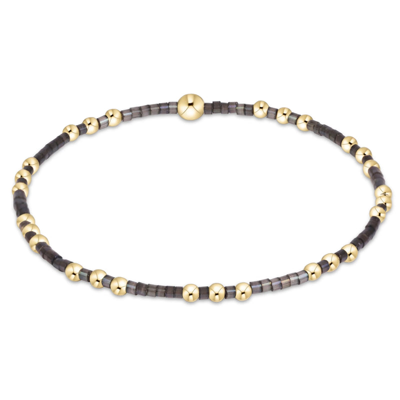 A beaded stretch bracelet featuring alternating polished gold-tone beads and dark gray faceted beads, with a larger central gold bead and a matching gold clasp, shown on a plain white background.