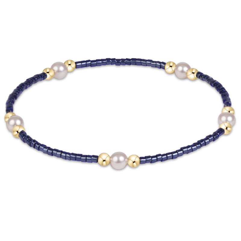 A beaded stretch bracelet featuring dark navy blue faceted beads, white freshwater pearls, and polished gold spacer beads, shown on a clean white background.