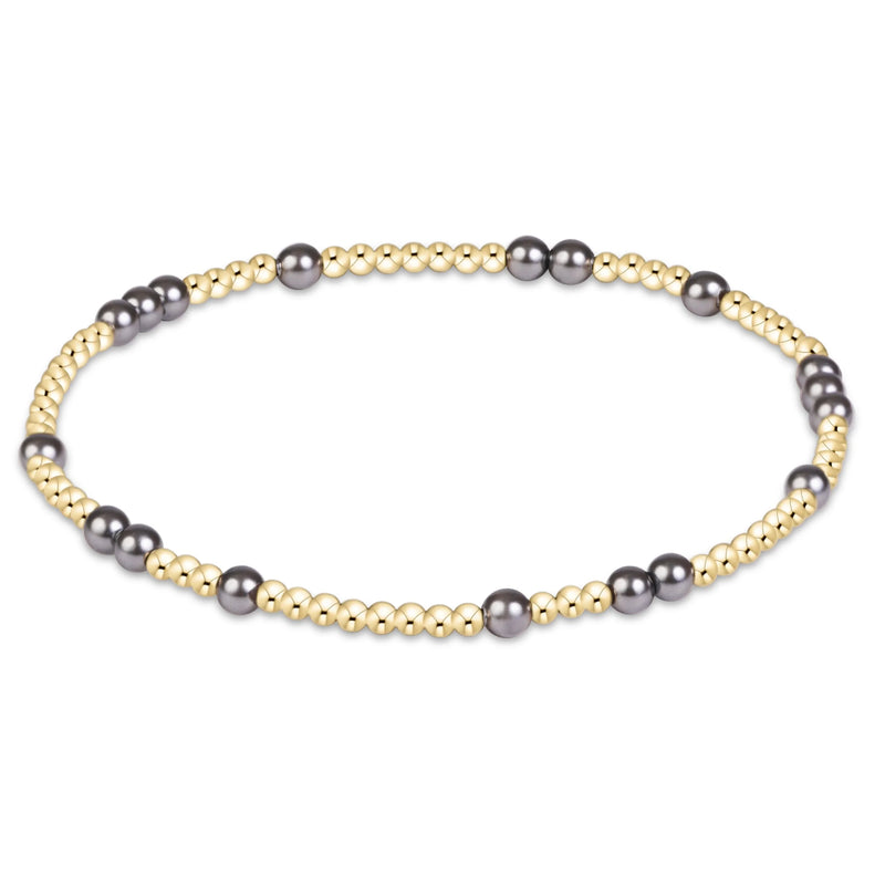 A beaded stretch bracelet featuring alternating strands of small gold-toned beads and larger dark gray freshwater pearls, displayed on a clean white background.