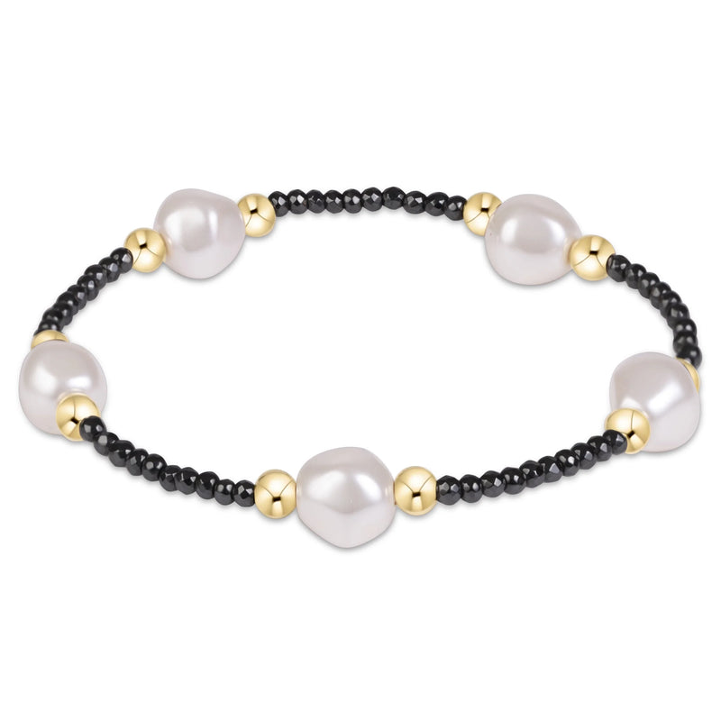 A beaded bracelet featuring large, irregular white freshwater pearls separated by small black beads and polished gold spacer beads, shown on a clean white background.