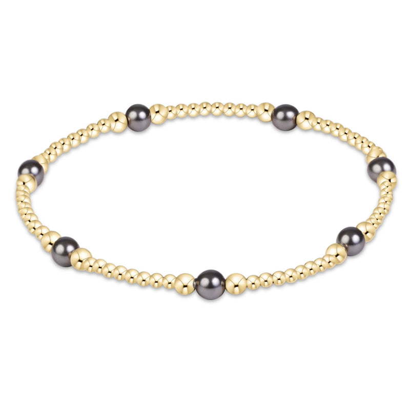 A beaded stretch bracelet featuring metallic gold beads and a few dark gray freshwater pearls, displayed on a clean white background.