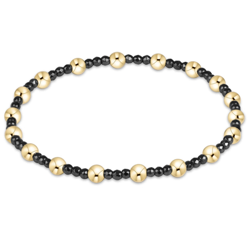 A beaded stretch bracelet featuring alternating large polished gold-tone round beads and smaller matte black round beads, displayed on a clean white background.
