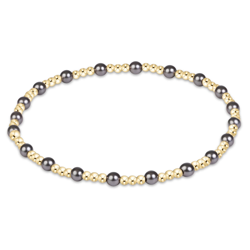 A beaded stretch bracelet featuring alternating large dark gray pearls and small polished gold beads, arranged in a circular shape on a plain white background.