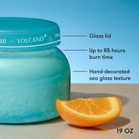 Blue Volcano candle jar with an orange slice on a light surface and blue background