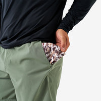Person wearing green pants with a patterned item in the pocket against a white background