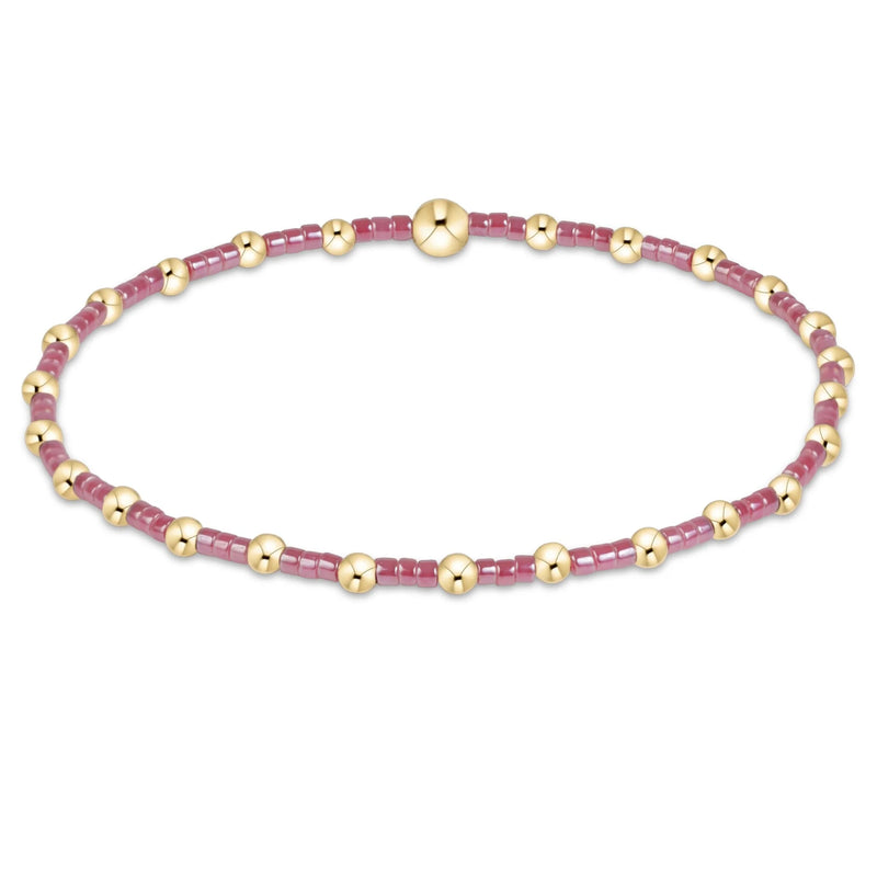 A delicate beaded bracelet featuring alternating translucent dusty pink beads and polished gold spacer beads, completed with a large round gold bead clasp at the top center, shown on a plain white background.