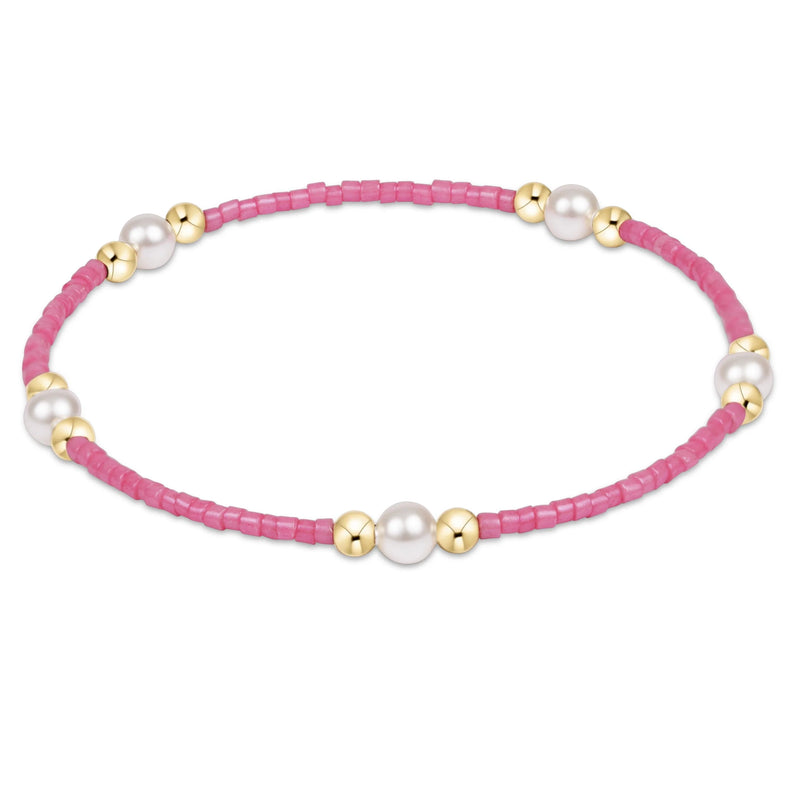 Pink beaded bracelet with pearls and gold accents on a white background