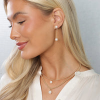 Woman wearing a delicate gold chain necklace featuring a single white freshwater pearl pendant.


