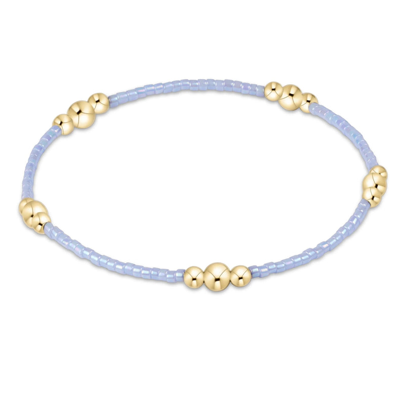 Bracelet with gold beads on a light purple cord against a white background