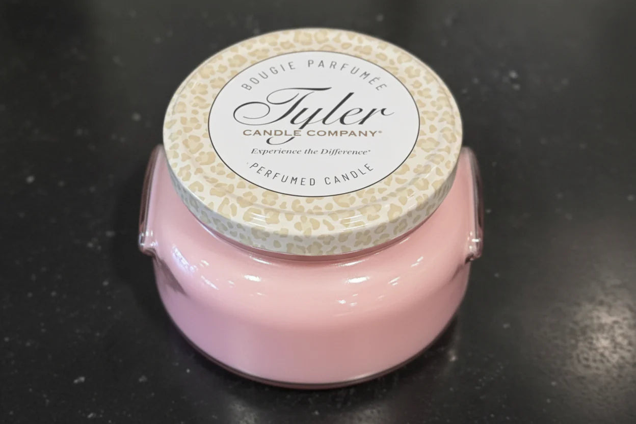 Pink candle with a white lid featuring 'Tyler Candle Company' on a black surface.
