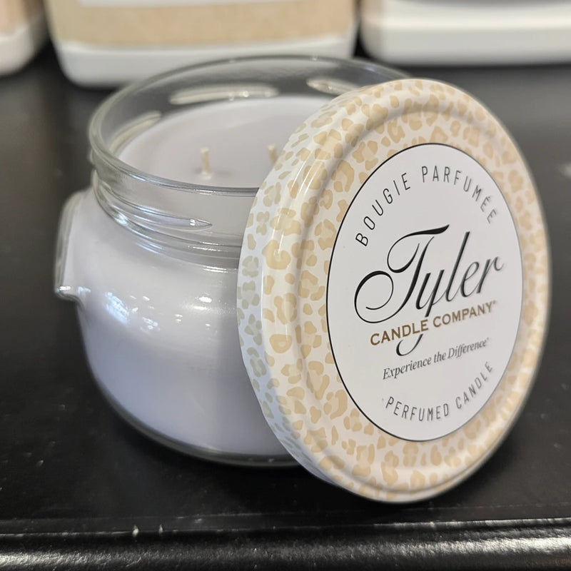 Grey candle in a glass jar with a decorative lid on a black surface, featuring the Tyler Candle Company branding.