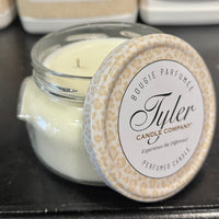 Blue candle in a glass jar with a decorative lid on a black surface, featuring the Tyler Candle Company branding.