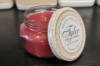 Red Candle in a glass jar with a decorative lid on a black surface, featuring the Tyler Candle Company branding.