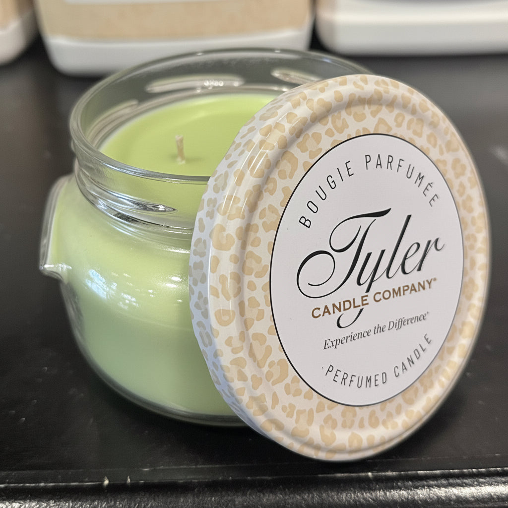  Green candle in a glass jar with a decorative lid on a black surface, featuring the Tyler Candle Company branding