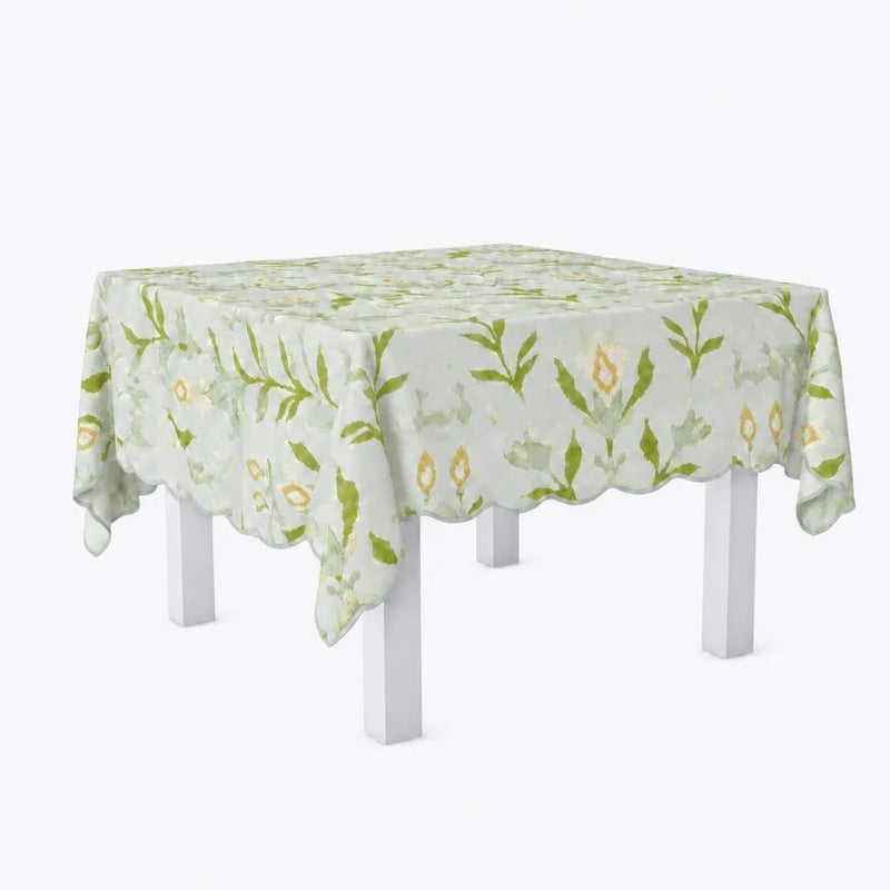 A square table covered with a light green and white tablecloth featuring a delicate botanical leaf pattern and scalloped edges, shown on a white table against a light gray background.