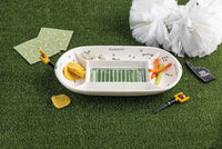A football-themed divided serving platter set on artificial grass with snacks, napkins, a pom-pom, and a toy whistle.