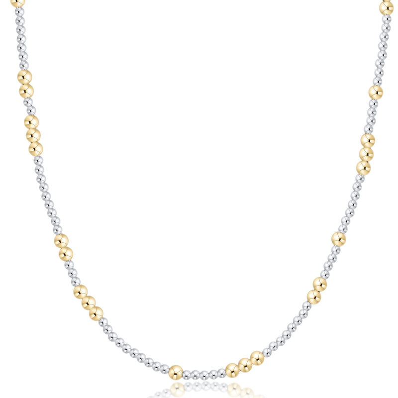 A delicate two-tone necklace featuring a silver-toned beaded chain accented with small gold-toned beads, displayed on a clean white background with a subtle reflection.