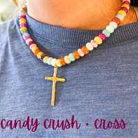 Colorful beaded necklace with a gold cross pendant on a person wearing a blue shirt.