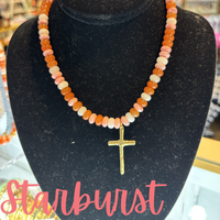 Necklace with a gold cross pendant on a black stand labeled 'Starburst'.
