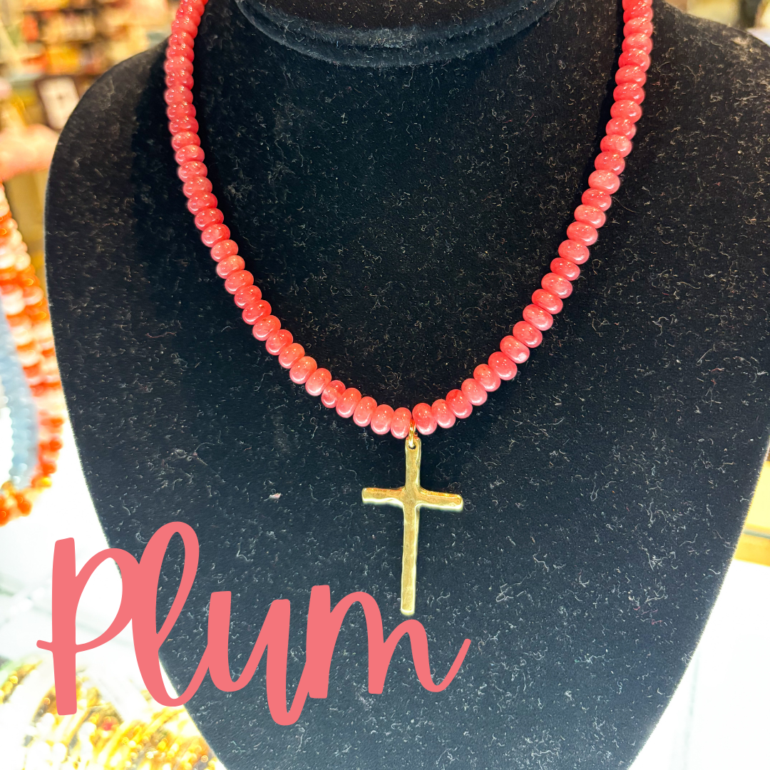 Necklace with red beads and gold cross pendant on a black stand with 'Plum' text.