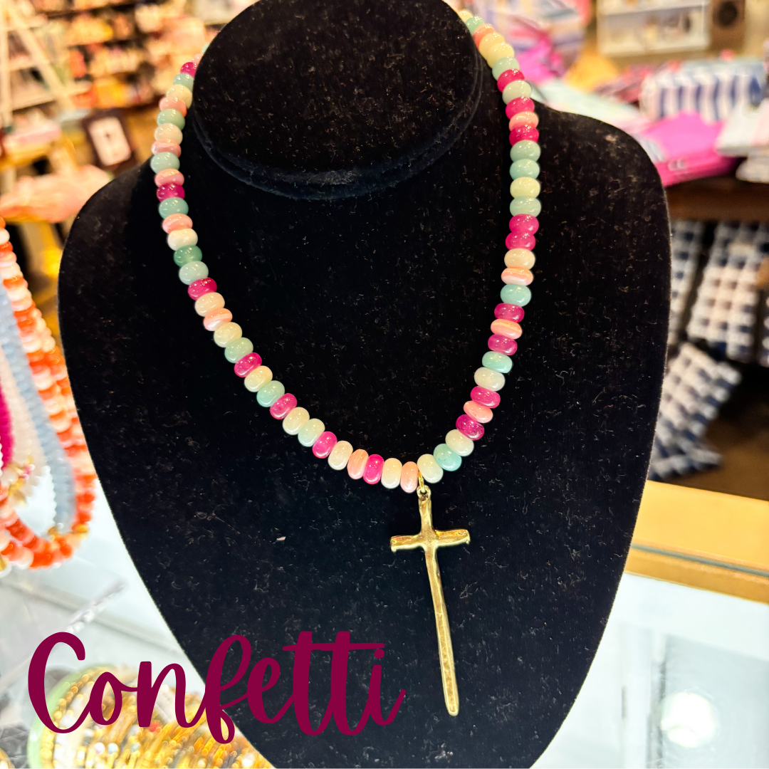 Colorful beaded necklace with a gold cross pendant on a black stand, with 'Confetti' text.