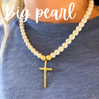 Pearl necklace with a gold cross pendant on a person wearing a blue shirt.
