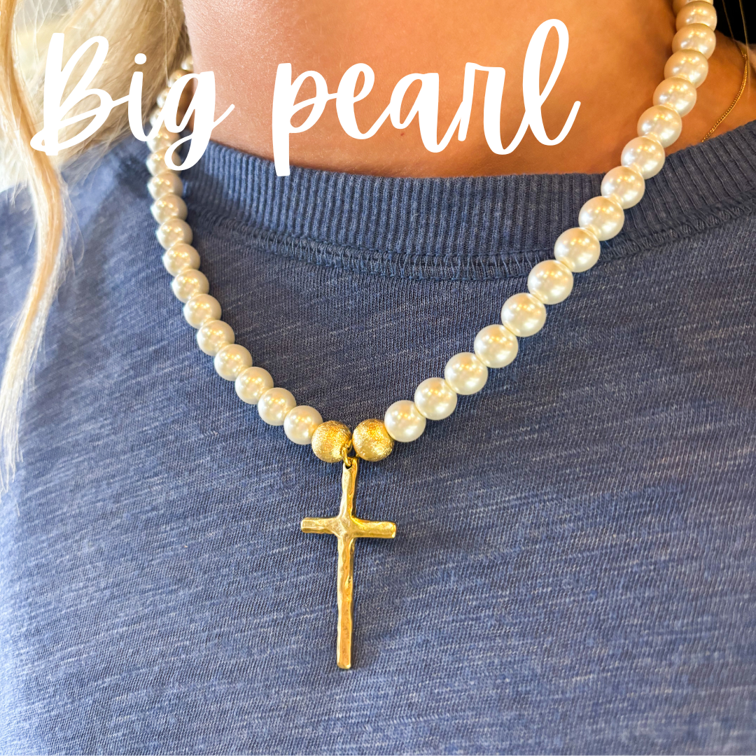 Pearl necklace with a gold cross pendant on a person wearing a blue shirt.