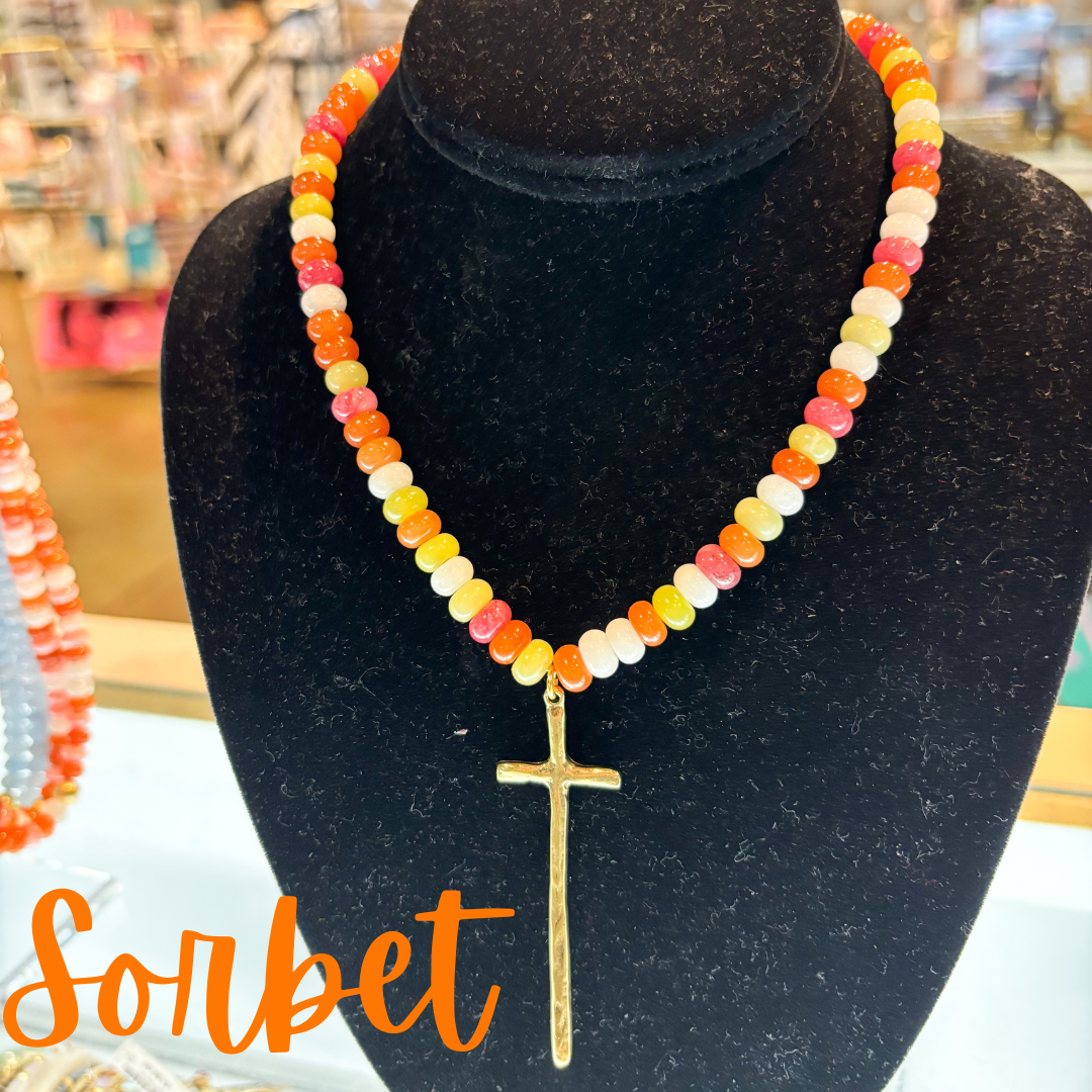 Necklace with colorful beads and a gold cross pendant on a black mannequin bust, with 'Sorbet' text.