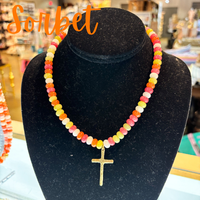 Colorful beaded necklace with a gold cross pendant on a black velvet stand, with 'Sorbet' text above.