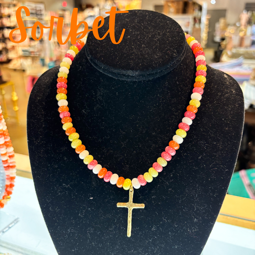 Colorful beaded necklace with a gold cross pendant on a black velvet stand, with 'Sorbet' text above.
