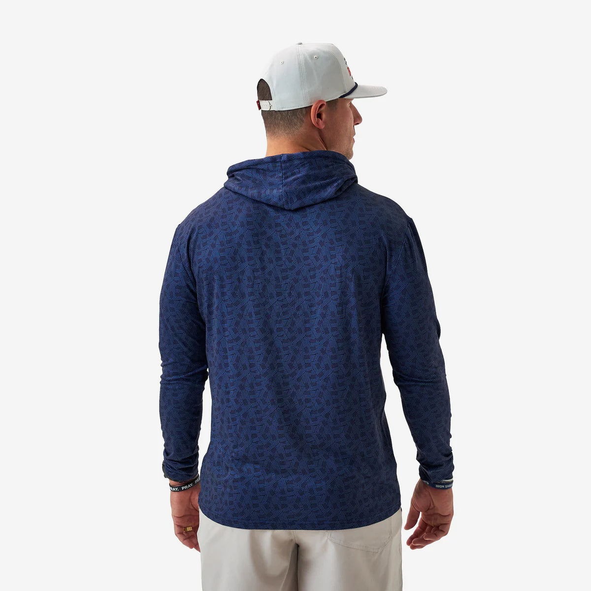 Man wearing a blue patterned hoodie and white cap on a light gray background