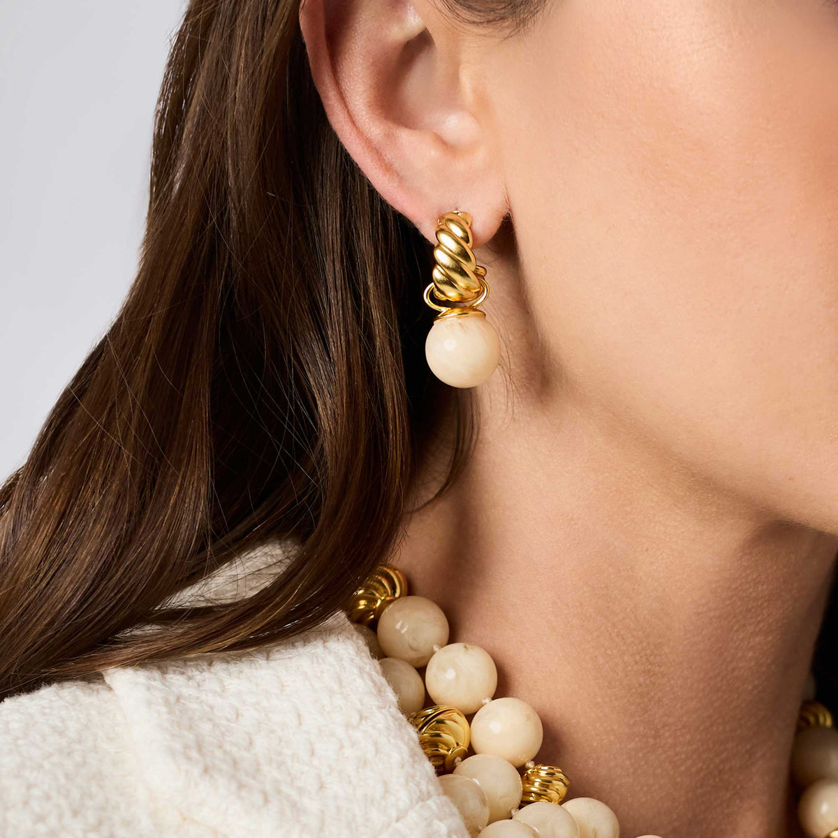 Close-up of a woman wearing gold and beige beaded earrings.