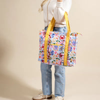 Person holding a colorful floral tote bag with yellow straps against a beige background