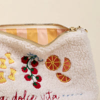 White pouch with embroidered fruit designs and 'a dolce vita' text on a beige background