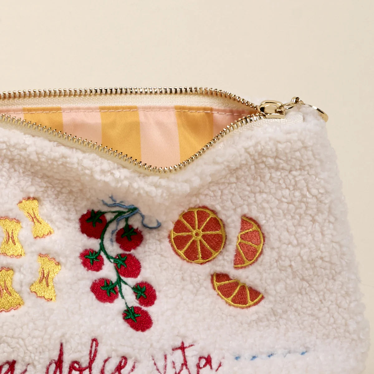 White pouch with embroidered fruit designs and 'a dolce vita' text on a beige background