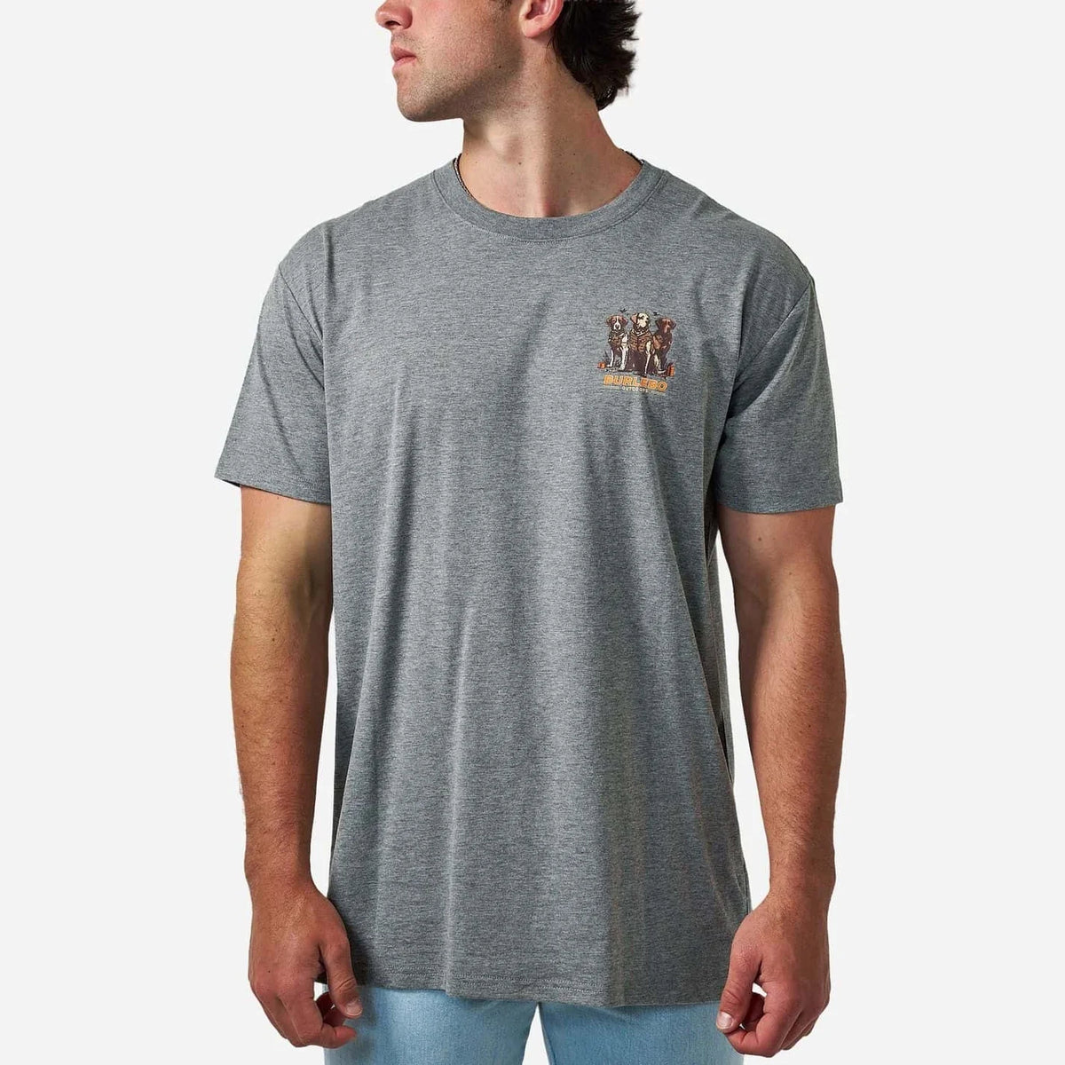 A man wearing a heather gray crewneck t-shirt with a small graphic on the left chest, paired with light blue jeans, against a light gray background.