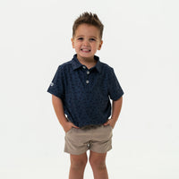 Child wearing a navy patterned shirt and beige shorts on a white background