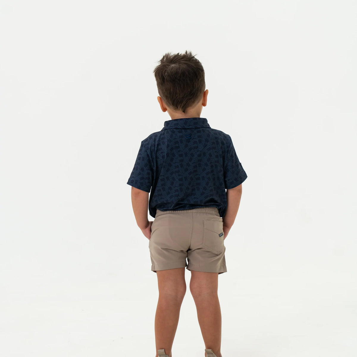 Child wearing a navy patterned shirt and beige shorts on a white background