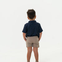 Child wearing a navy patterned shirt and beige shorts on a white background
