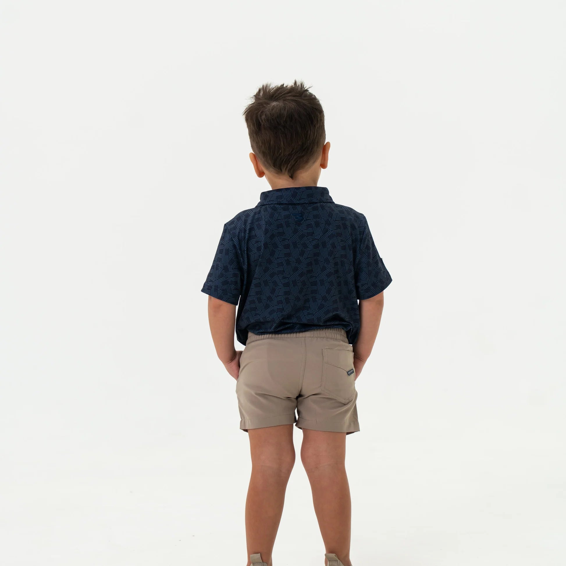 Child wearing a navy patterned shirt and beige shorts on a white background