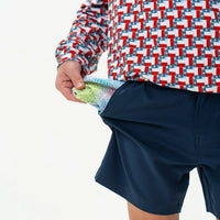 Person wearing a red, white, and blue patterned shirt and navy shorts holding money.