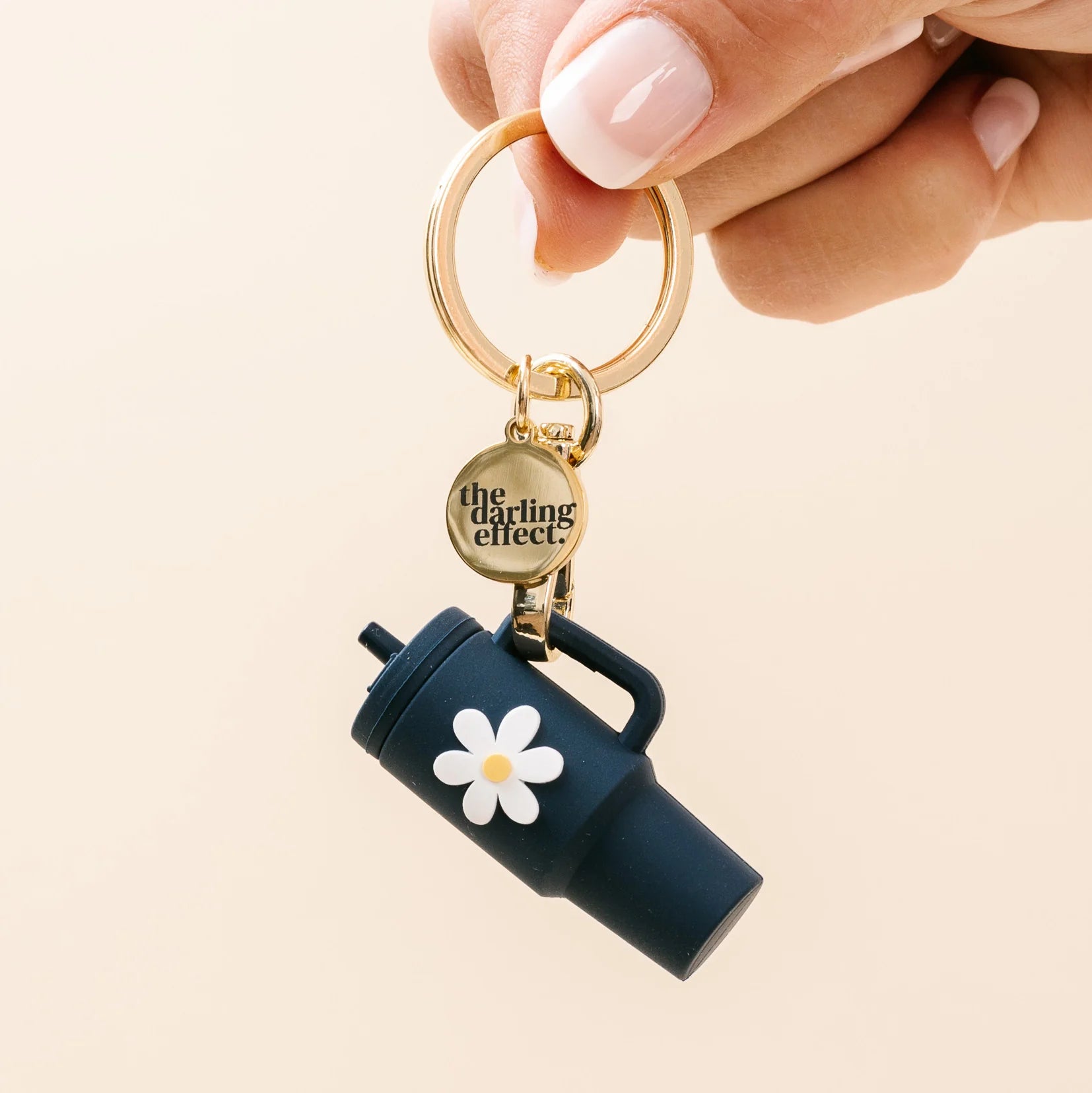 Keychain with a navy blue mug design and white flower, held by a hand against a beige background.