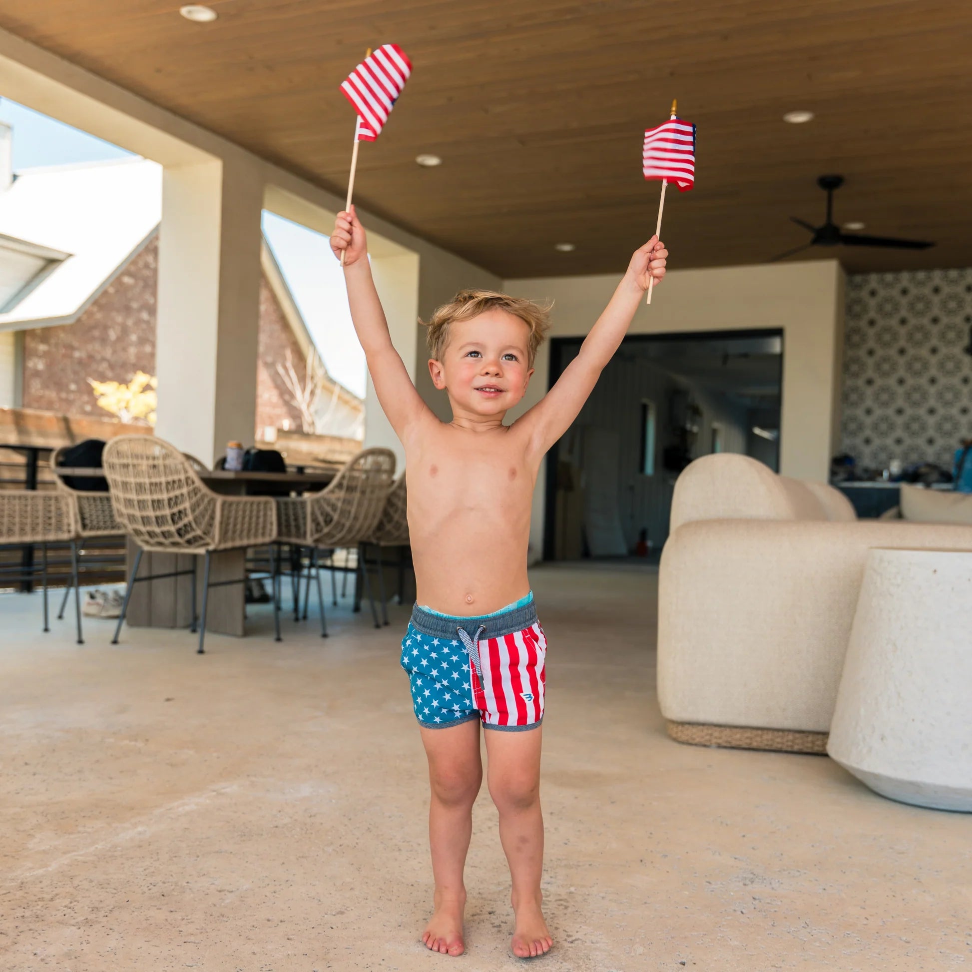 Child holding two small American flags in an outdoor setting
