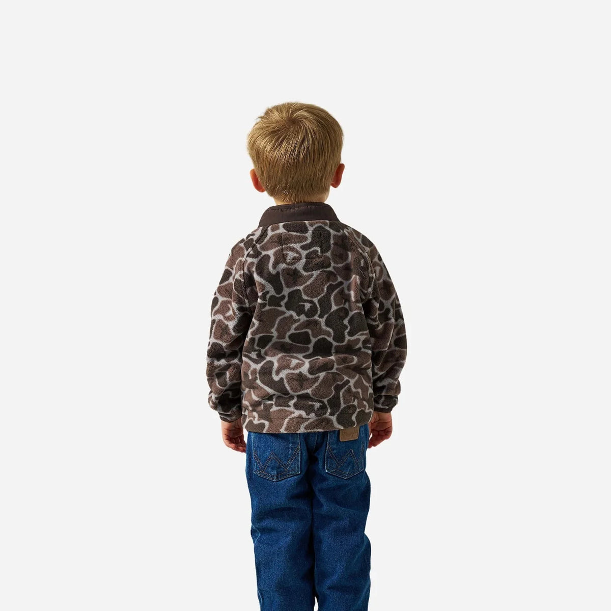 A young boy viewed from behind wearing a brown and beige camouflage pattern fleece jacket and blue jeans, standing against a plain light gray background.