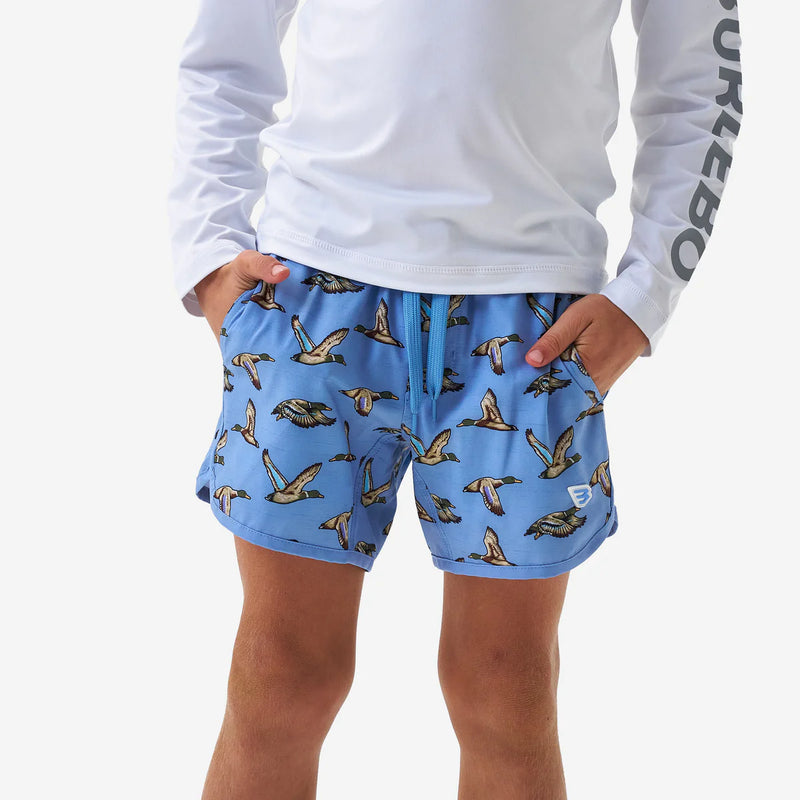 Person wearing blue shorts with duck pattern and white long-sleeve shirt on a light gray background