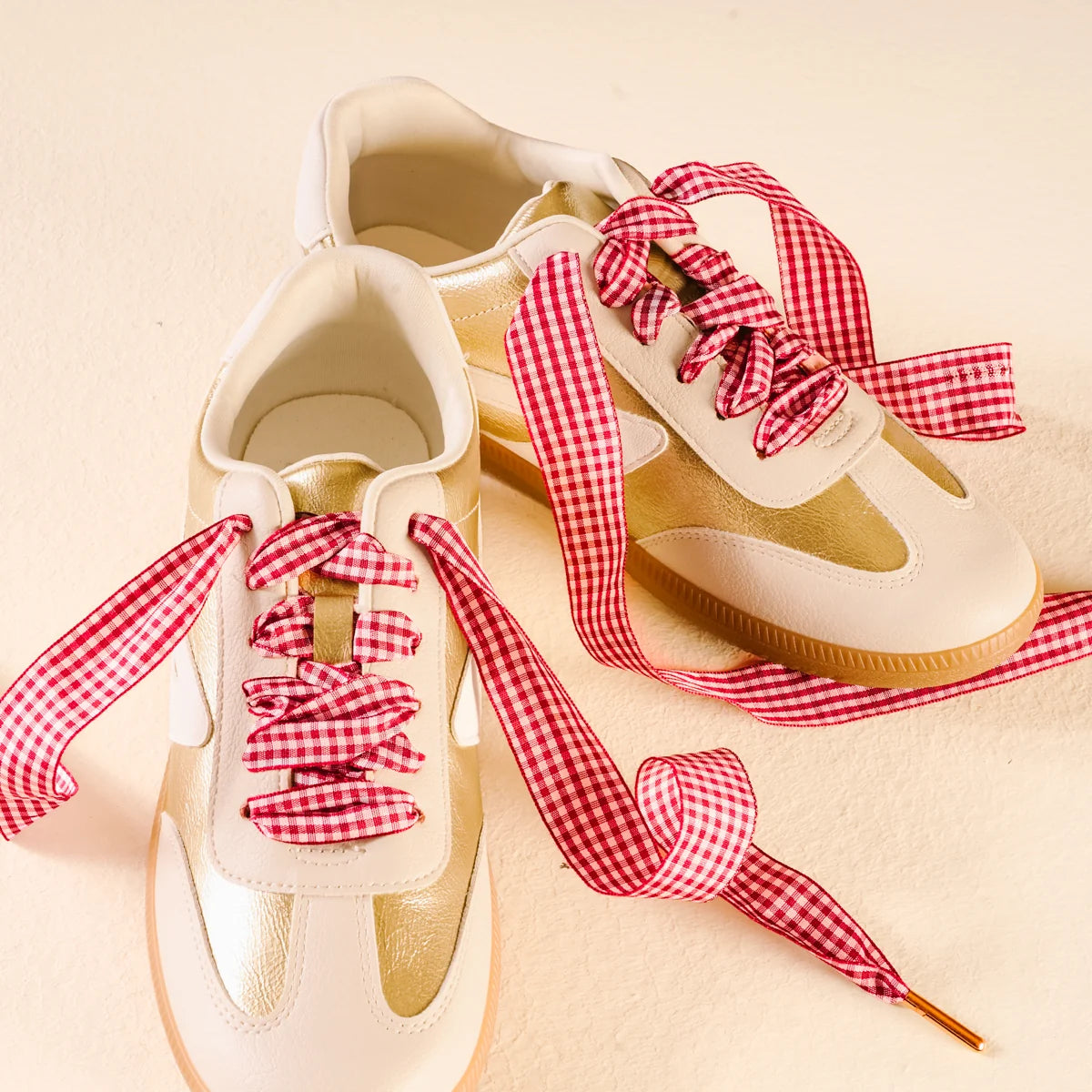 White sneakers with red and white checkered laces on a beige background