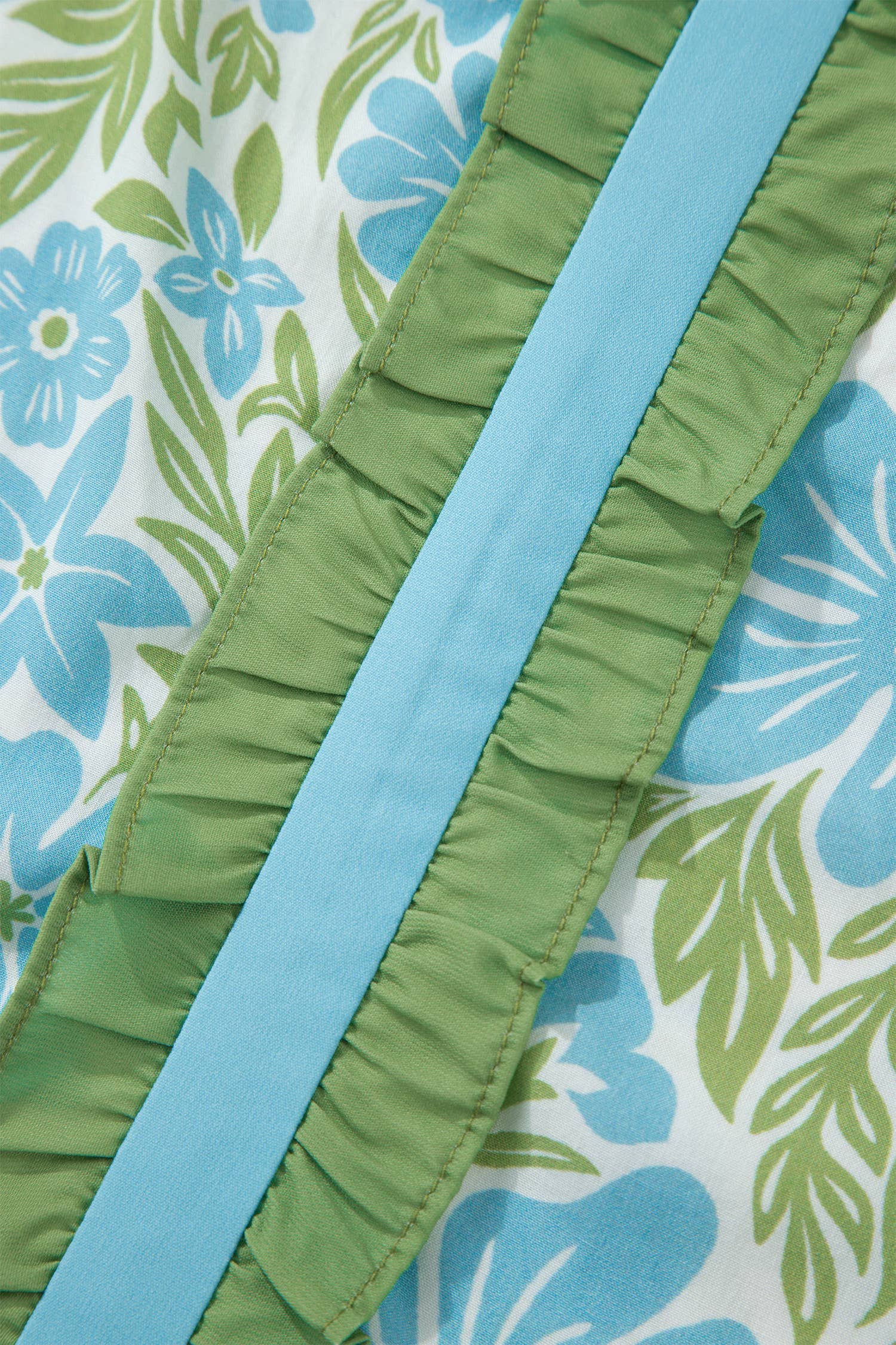 Close-up of green ruffled fabric with blue trim on a floral background