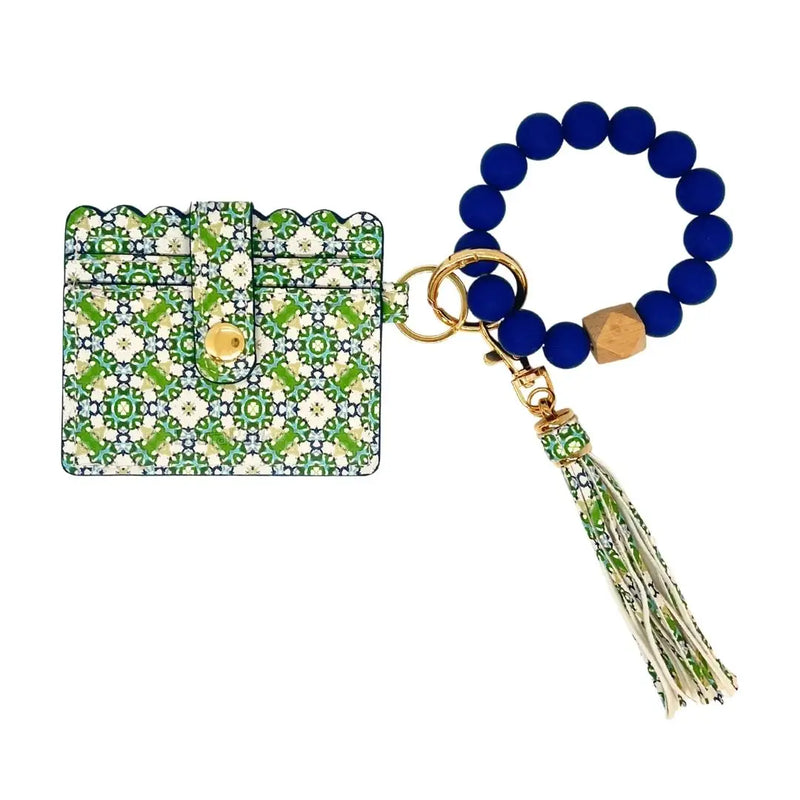 A card holder wallet with a green and white geometric tile pattern, featuring a gold snap button, attached to a beaded keychain with blue beads, gold hardware, and a matching tassel on a white background.