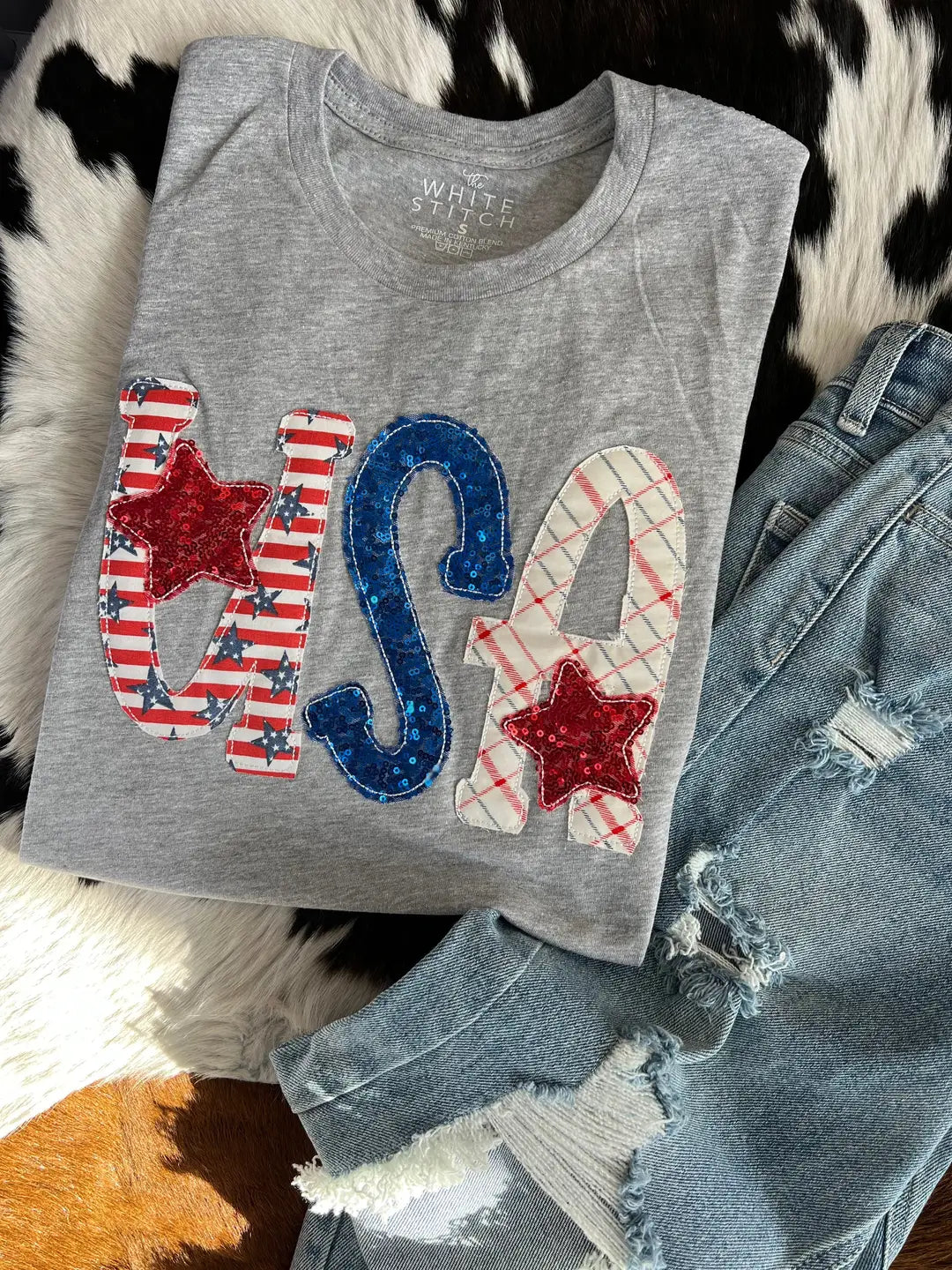 Gray tank top with 'USA' design on a textured surface with jeans.
